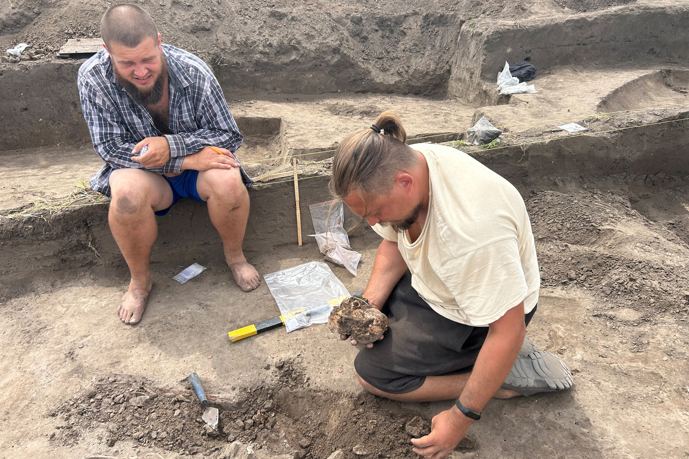 Руководитель Островского отряда Дмитрий Дяченко и сотрудник Института археологии НАН Украины Никита Шекера готовят к упаковке череп ребенка из захоронения XI века на археологическом раскопе «Остров». Поросье, Киевская область, Украина. Июль 2026 года. Фото: Дмитрий Дурнев / «Новая газета Европа»