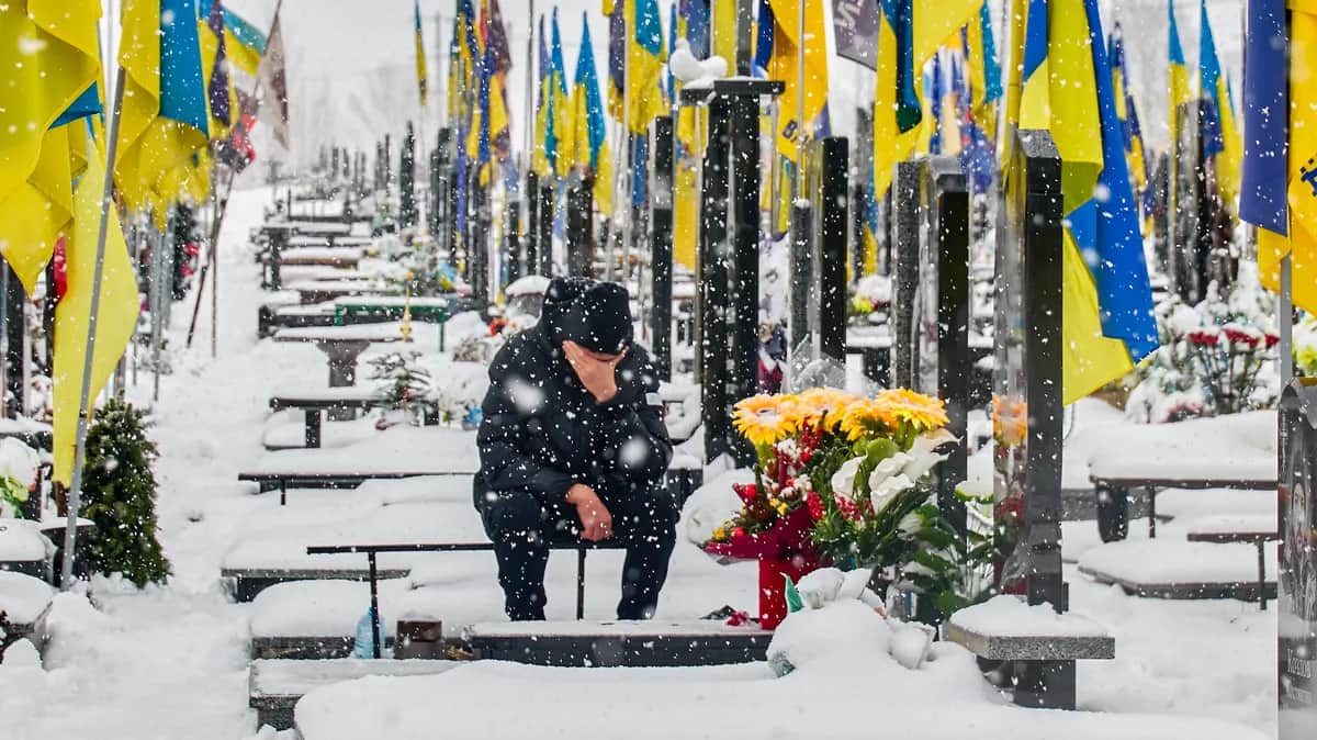 A mourner sits by the side of a grave in Kharkiv’s Alley of Heroes, 28 December 2025. Photo: EPA / SERGEY KOZLOV