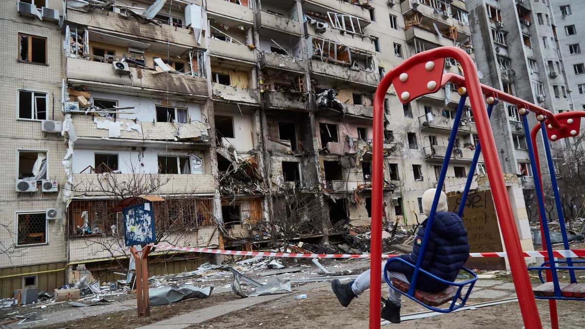Ребенок на качелях возле жилого дома, поврежденного ракетой, 25 февраля 2022 года в Киеве, Украина. Фото: Pierre Crom/Getty Images