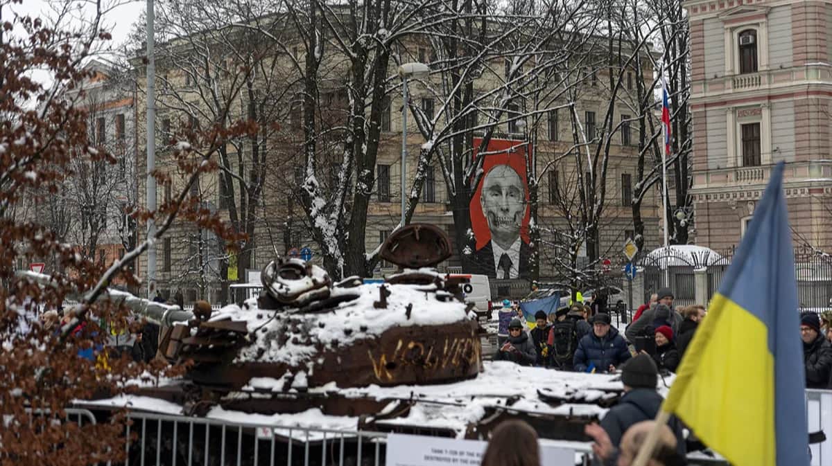 A burnt-out Russian tank from Ukraine against a backdrop of Putin near the Russian embassy in Riga, Latvia, 24 February 2023. Photo: Vladislav Dokshin / Novaya Europe