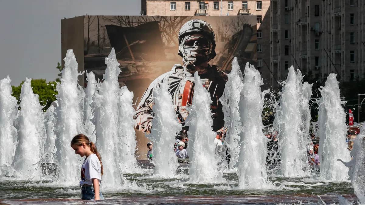 A young Russian cools down in a Moscow water fountain in front of a poster depicting a Russian soldier, 29 May 2024. Photo: Yuri Kochetkov / EPA-EFE