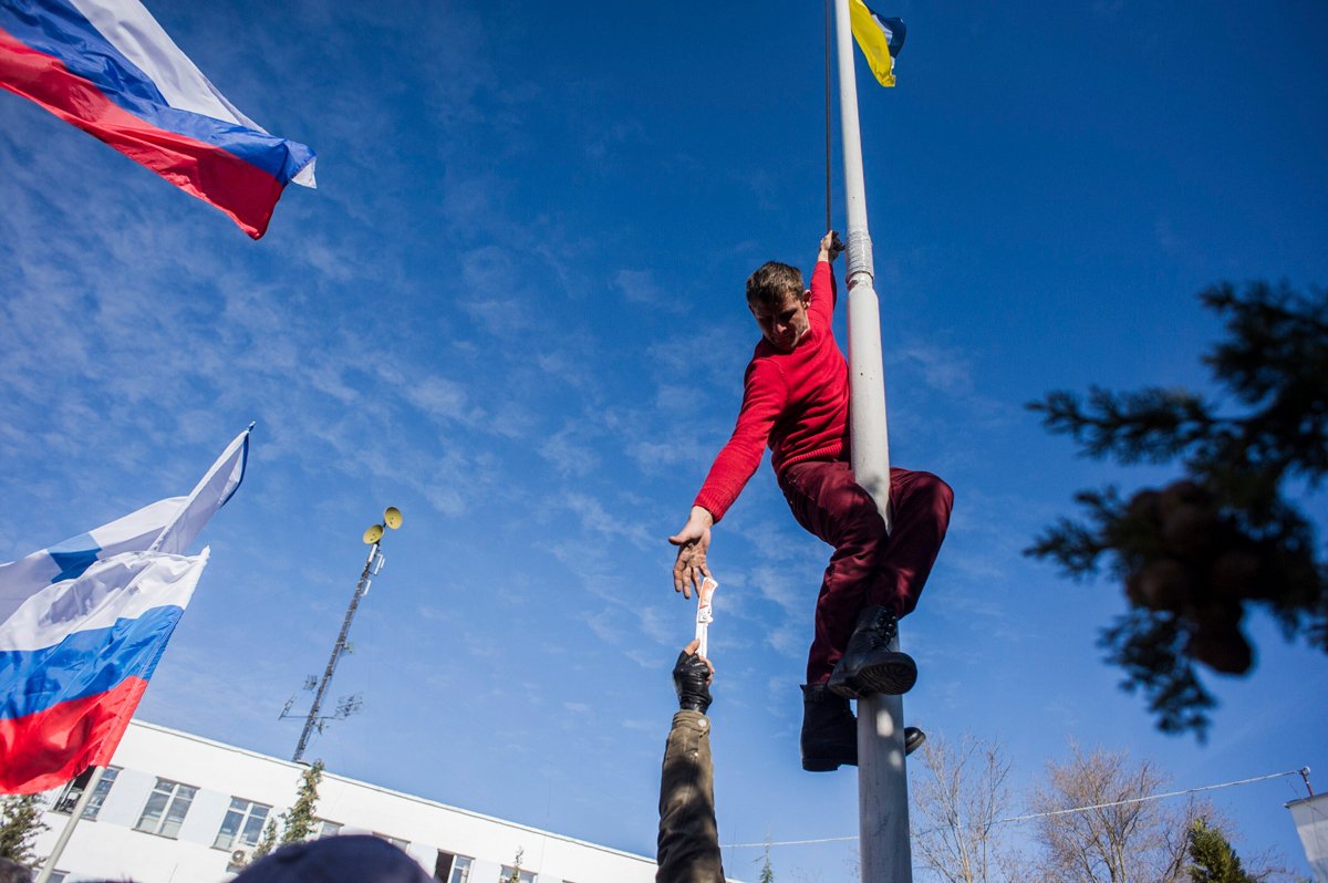 Участник пророссийского отряда самообороны тянется за ножом, чтобы снять украинский флаг в Севастополе, 19 марта 2014 года. Фото: AP Photo / Scanpix / LETA